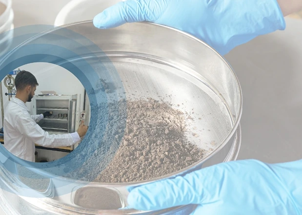 Profissional em laboratório realizando análise de material pulverizado com peneira metálica e equipamentos de ensaio.